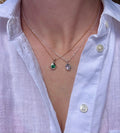 Two Birthstone Droplet Pendants worn layered with a white linen shirt: bronze with an emerald on a gold filled chain, and sterling silver with an alexandrite