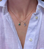 Two Birthstone Droplet Pendants worn layered with a white linen shirt: bronze with an emerald on a gold filled chain, and sterling silver with an alexandrite