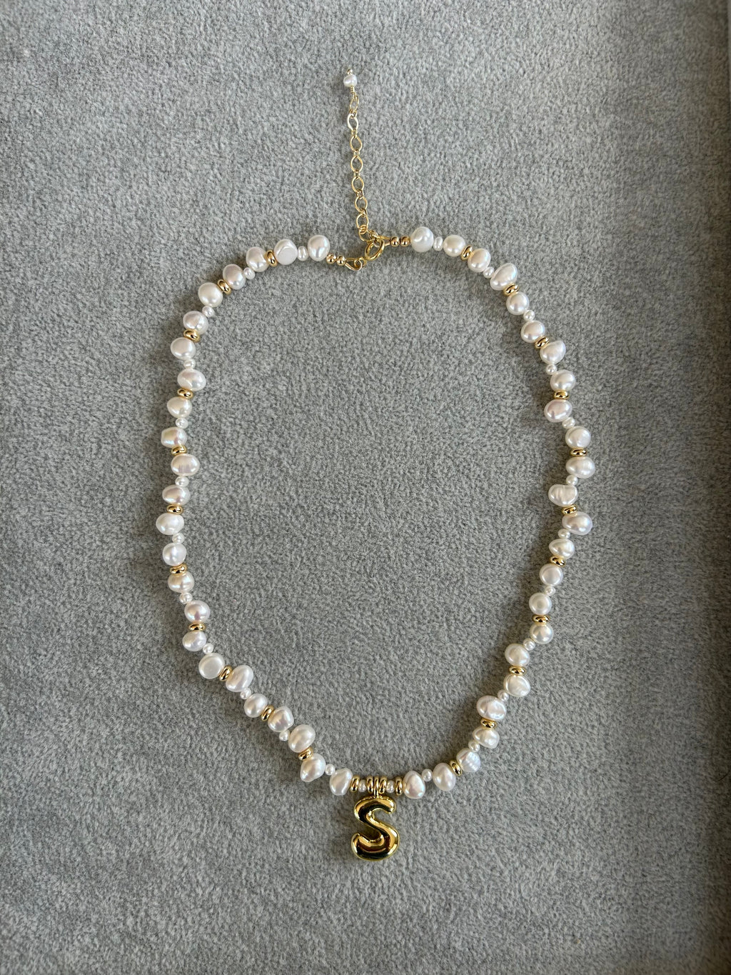 Pearl necklace with a gold 'S' charm on a gray background