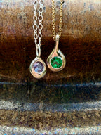 Close-up of handmade Birthstone Droplet Pendants: sterling silver set with an alexandrite and bronze set with an emerald in a fine silver bezel on a gold filled chain