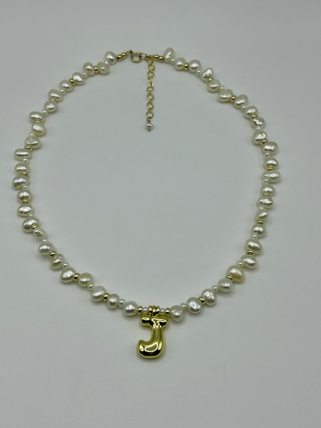 Pearl necklace with a gold letter 'J' charm on a light gray background
