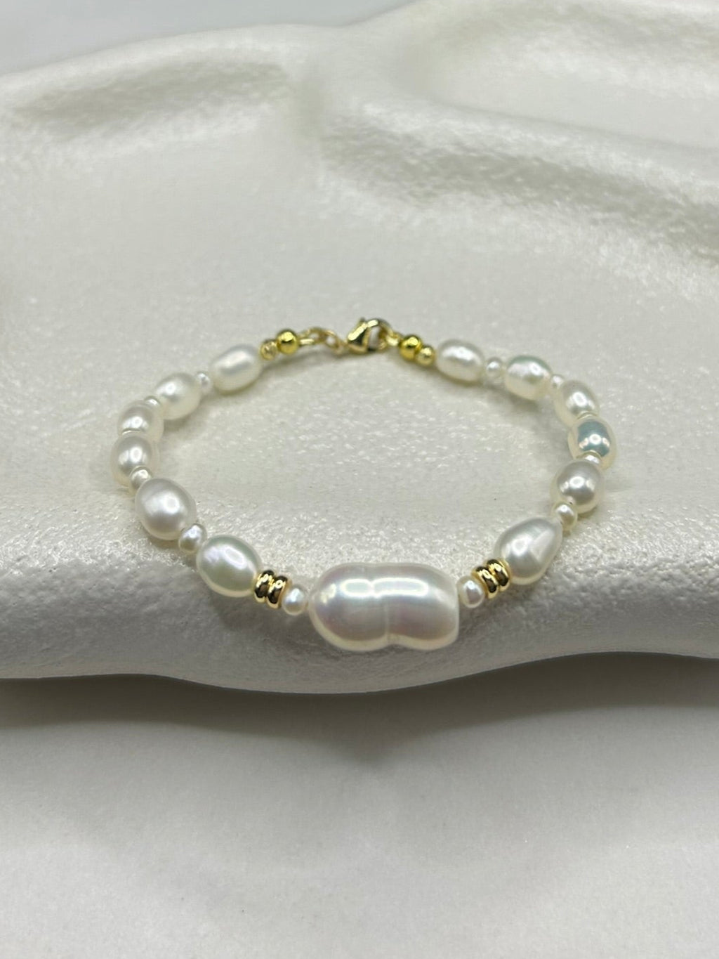 Pearl bracelet with gold accents on a white cushion against a dark background